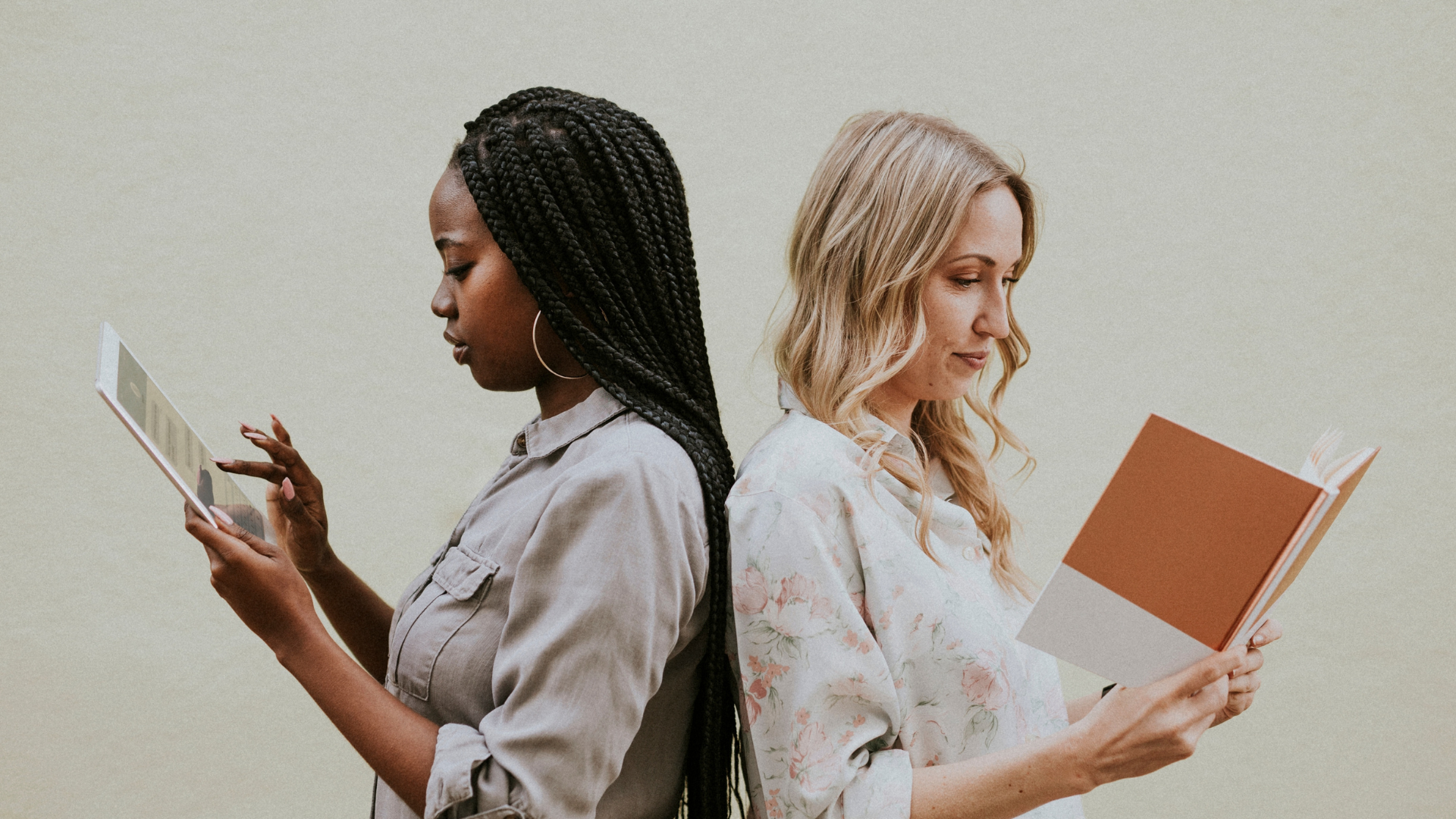 Two women back to back, one reading, one working on a tablet. Business and friendship