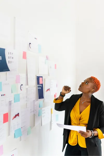 A professional black marketing strategy consultant reviewing a wall filled with notes for her marketing strategy